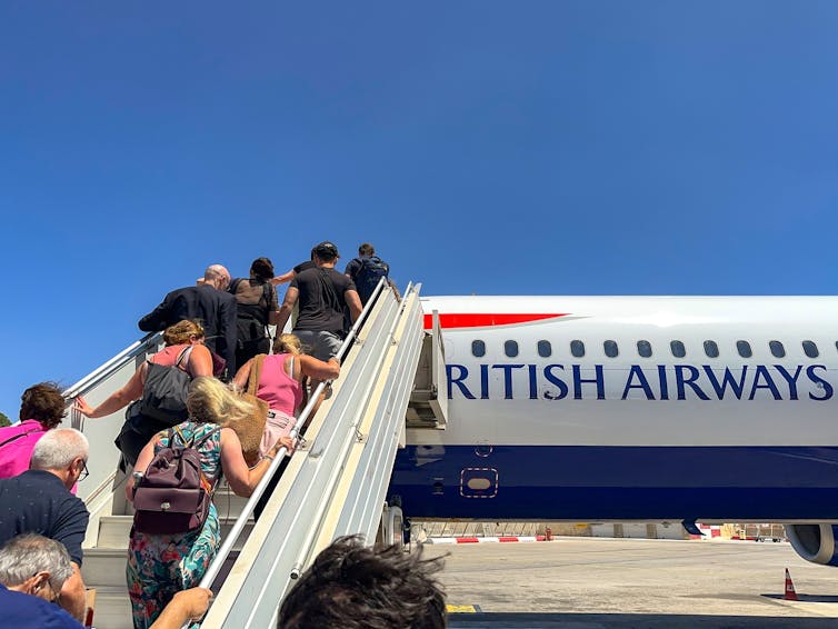 Tourists climbing an escalator onto an aeroplane.