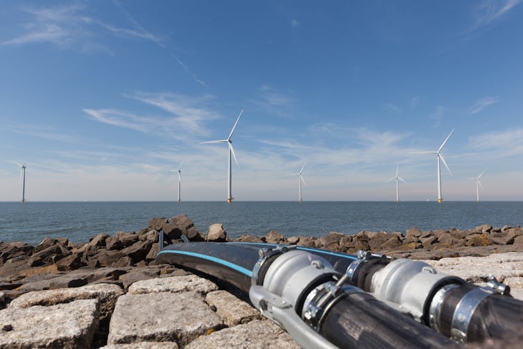 Two large cables running from the shore with offshore wind turbines on the horizon.