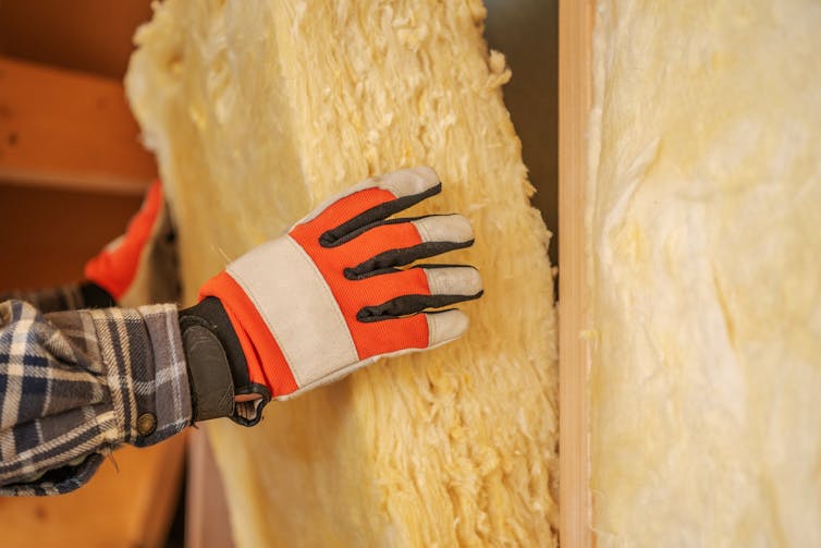 builder's hands in gloves holding yellow wall insulation